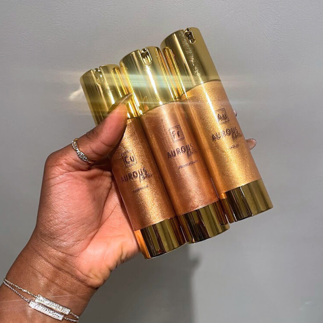 Hand holding three gold and bronze bottles with 'Aurous' branding against a gray background